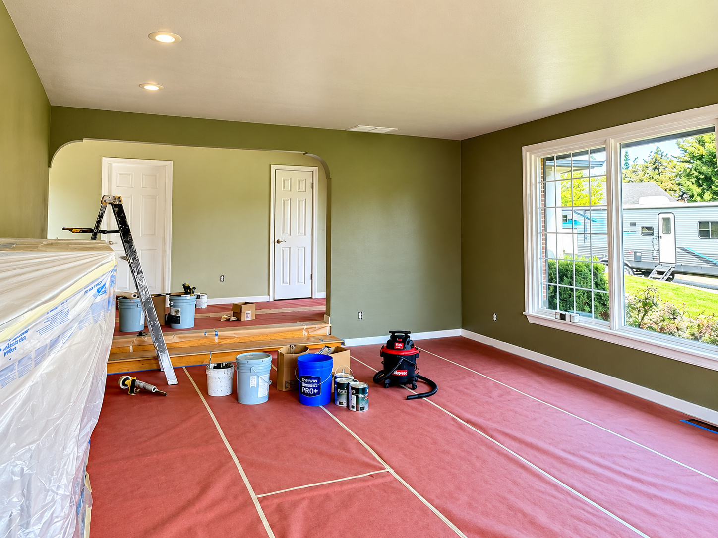 Olive-green interior walls in a residential painting project with protected floors and painting equipment.