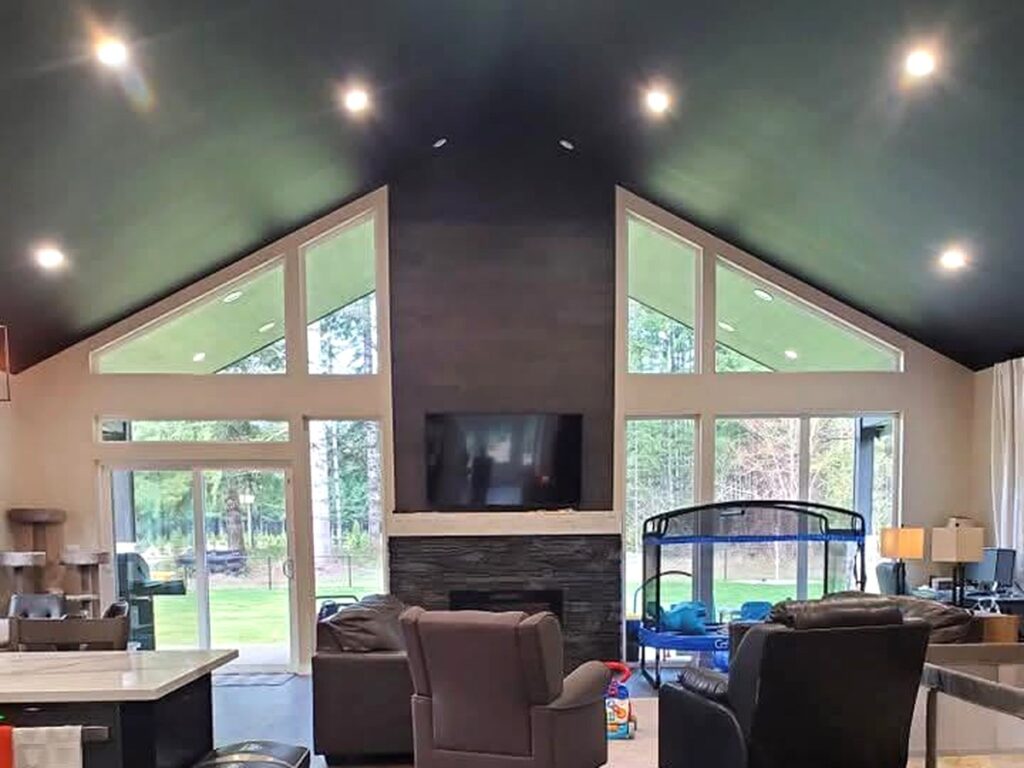 Dark painted vaulted ceiling with recessed lighting in a living room featuring large windows and a fireplace.